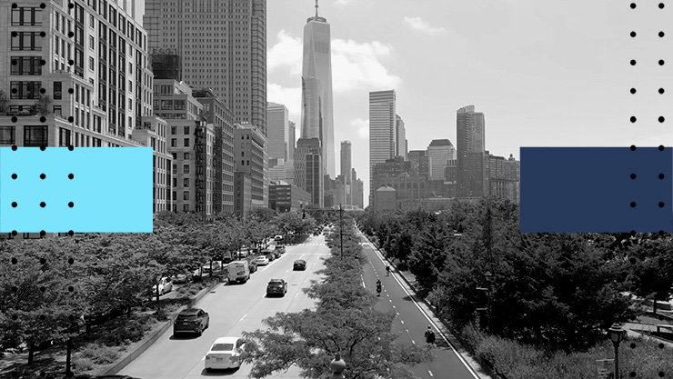 Wide angle view of a tree-lined avenue in New York City, with traffic moving toward One World Trade Center and the Lower Manhattan skyline in the background.