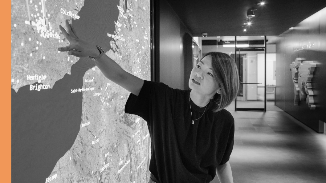 Woman gesturing toward a large digital map display in a modern office space